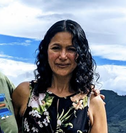 Norma Alvarez, Venezuelan spiritual practitioner, smiling outdoors with mountains and sky in background, wearing floral patterned top